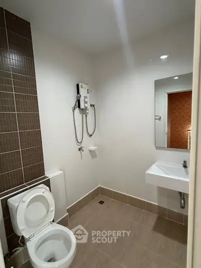 Modern bathroom with wall-mounted electric shower unit, pristine white sanitary ware, and contrasting brown tiles, offering a clean and functional space.