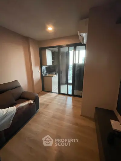 Cozy living room with wooden flooring and glass doors leading to a modern kitchen.