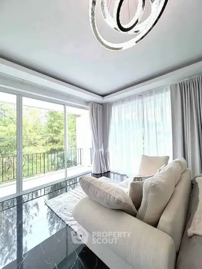 Elegant living room with modern chandelier and large windows overlooking greenery.