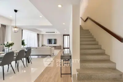 Modern open-plan living room with dining area and staircase, featuring elegant decor and ample natural light.