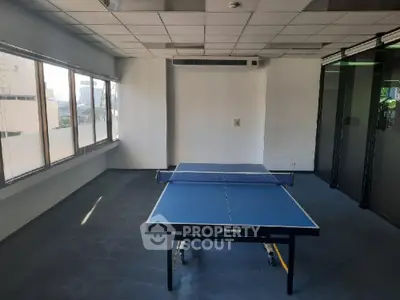 Spacious and versatile room with ample natural light, perfect for a recreational area or a modern office space, featuring large windows and a ping pong table.