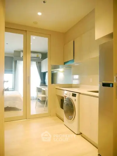 Modern compact kitchen with sleek appliances and a glimpse into the cozy bedroom, perfect for urban living in a space-efficient apartment.