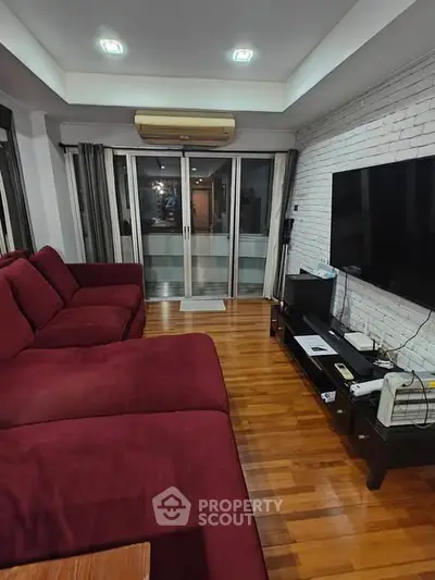 Spacious living room with red sofa and large TV, featuring wooden flooring and modern decor.