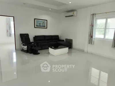 Spacious living room with modern black sofa and massage chair, bright natural light from large window.
