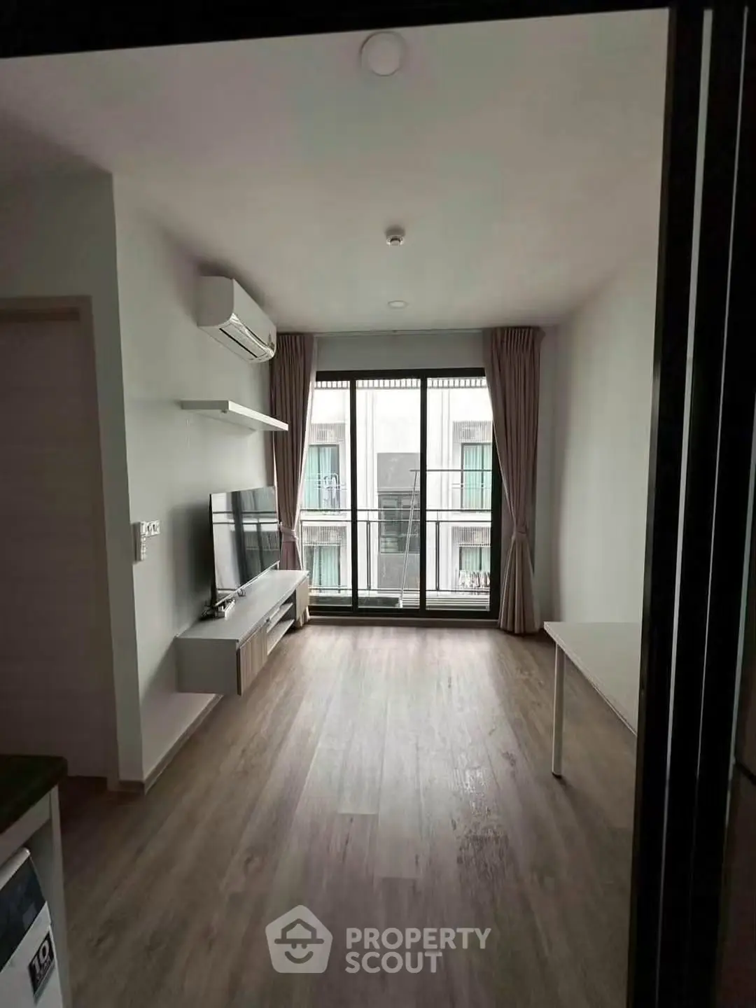 Modern living room with large window and balcony view, featuring sleek flooring and minimalist decor.
