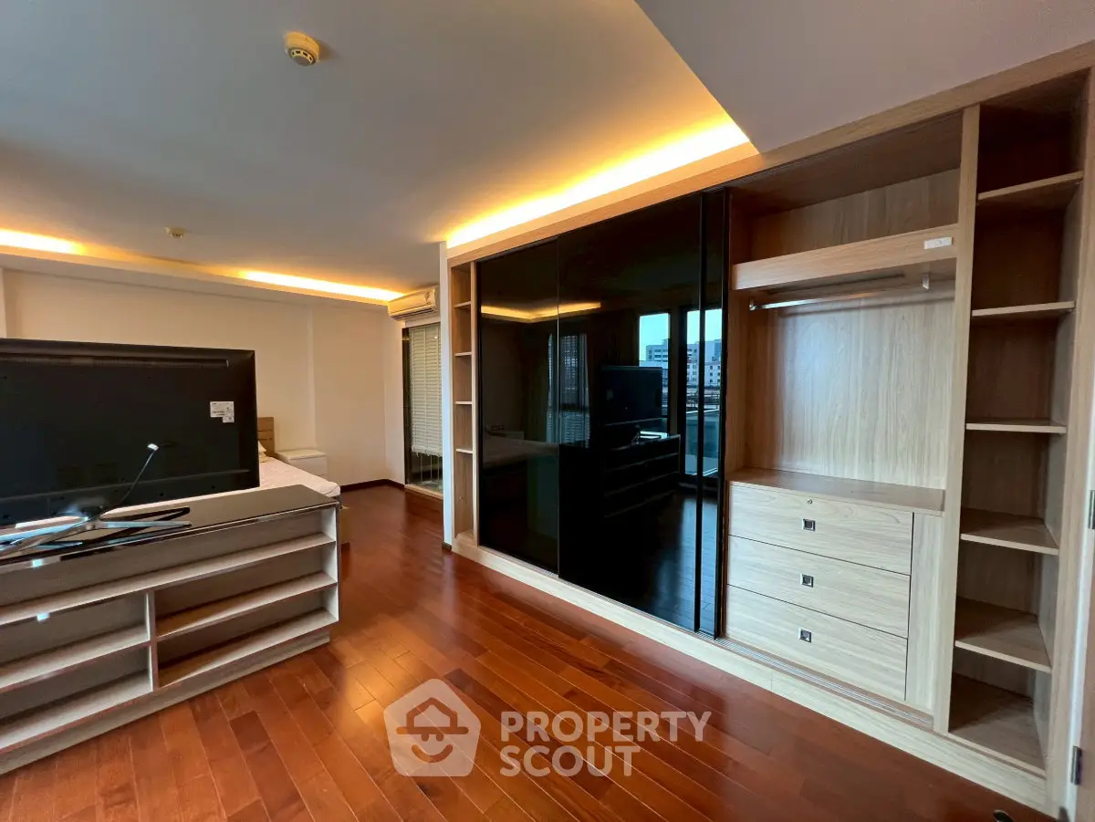 Spacious living room with wooden flooring and built-in storage, featuring modern lighting and large TV setup.