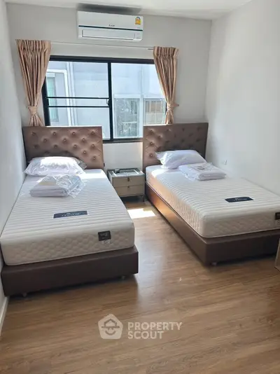 Cozy twin bedroom with modern decor and ample natural light, perfect for comfortable living.