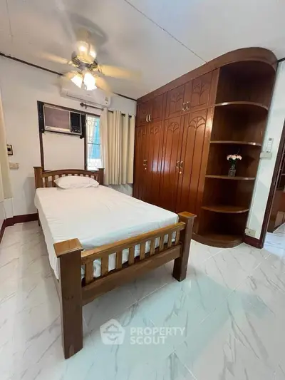 Cozy bedroom with wooden furniture and built-in wardrobe, featuring a ceiling fan and air conditioning.