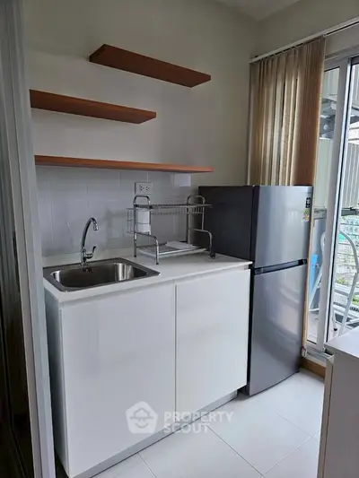 Modern compact kitchen with sleek cabinetry and stainless steel fridge in a bright apartment.