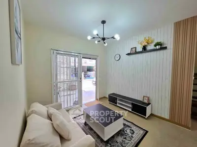 Cozy living room with modern decor and natural light, featuring a stylish chandelier and comfortable seating.