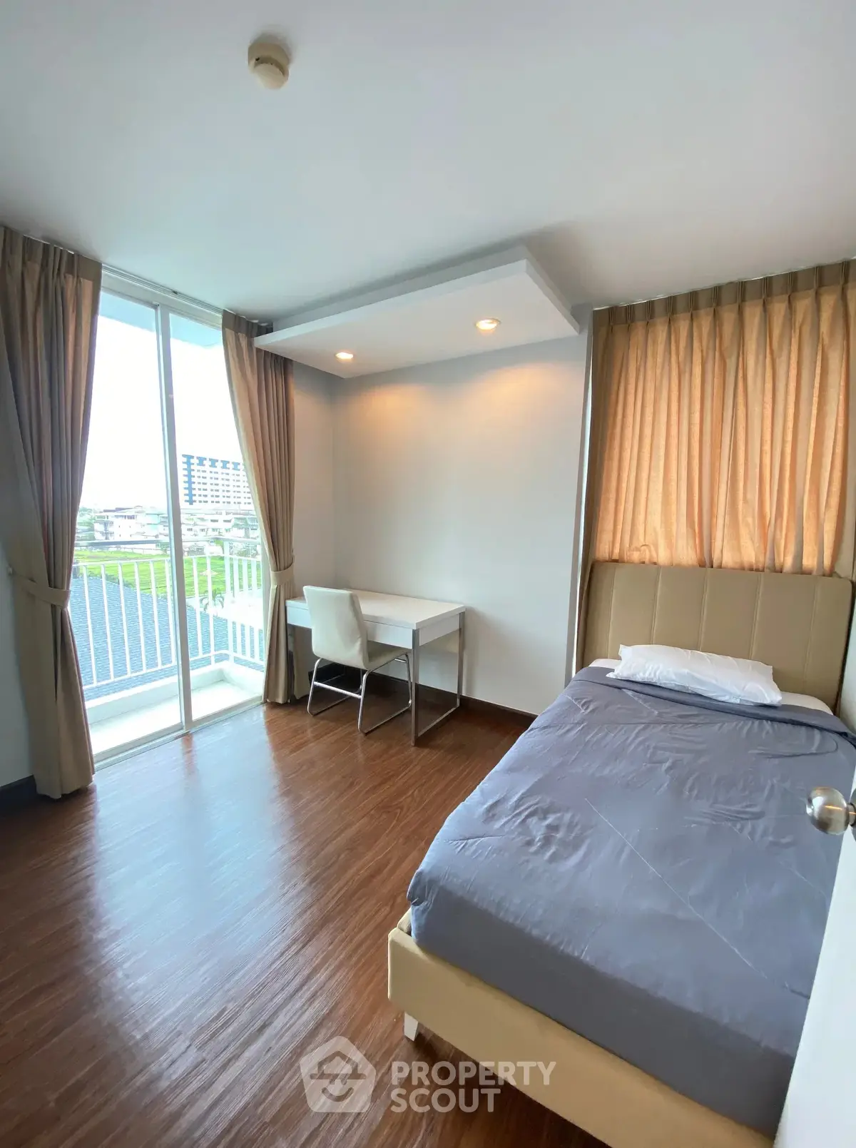 Modern bedroom with balcony view, featuring sleek wooden flooring and cozy study area.