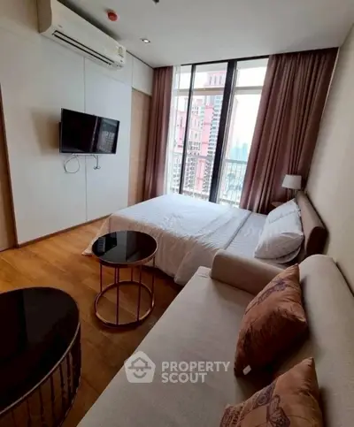 Modern bedroom with city view, featuring cozy bed, wall-mounted TV, and stylish seating area.