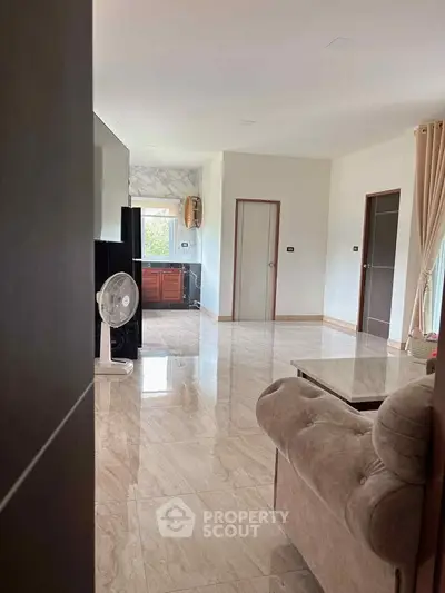 Spacious living room with elegant marble flooring and cozy sofa, leading to a modern kitchen.