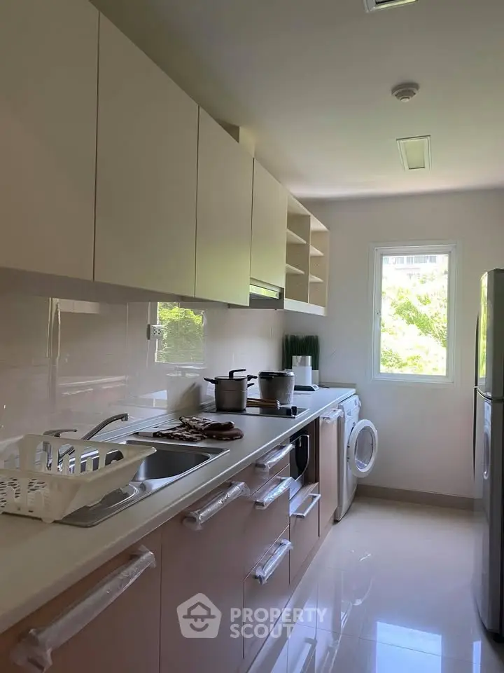 Modern kitchen with sleek cabinetry, washing machine, and ample natural light from window.