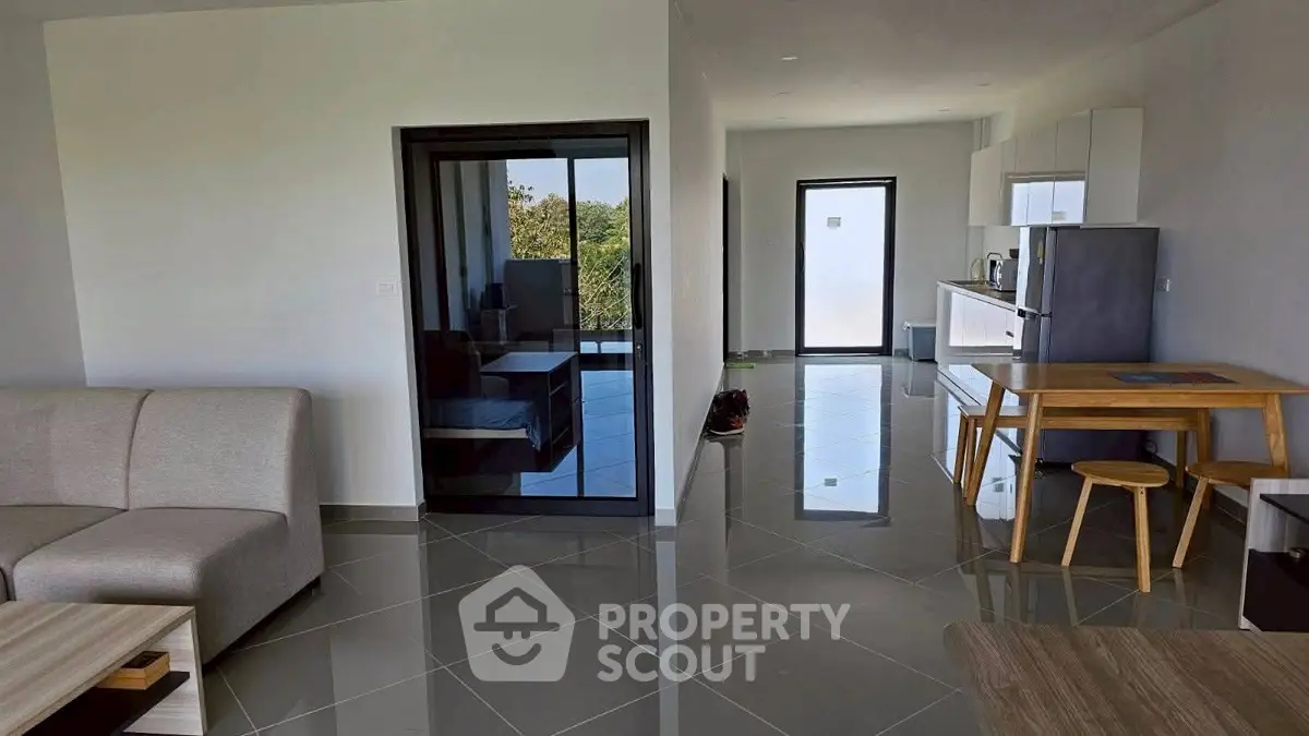 Modern open-plan living room with sleek kitchen and glossy tiled floors, featuring a cozy sofa and dining area.