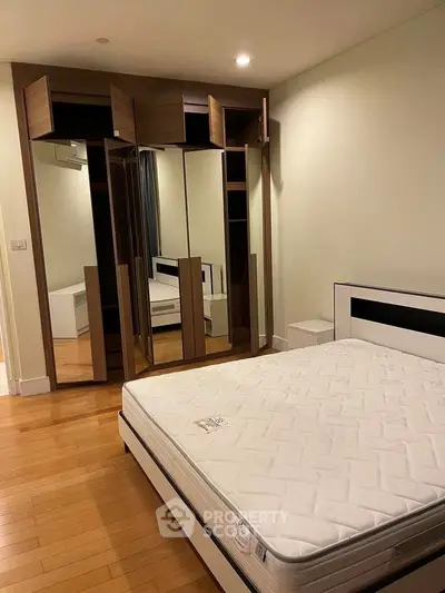 Spacious bedroom with wooden flooring and mirrored wardrobe in modern apartment.