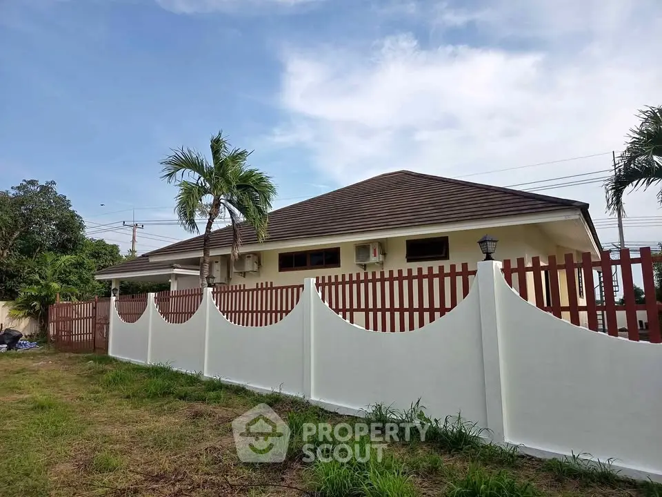 Charming single-story house with a red fence and lush greenery, perfect for serene living.