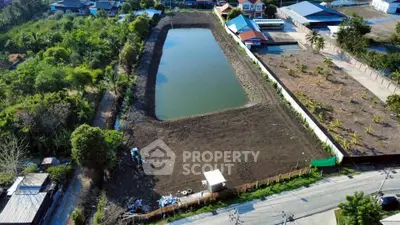 Aerial view of a large plot with a pond, surrounded by greenery and nearby buildings, ideal for development.
