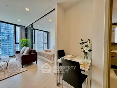 Modern open-plan living room with dining area and bedroom in a high-rise apartment with city views.