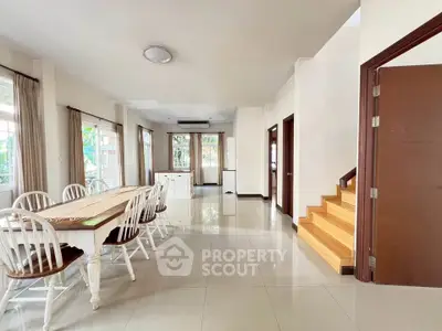 Spacious dining area with elegant wooden table and chairs, bright natural light, and modern staircase.