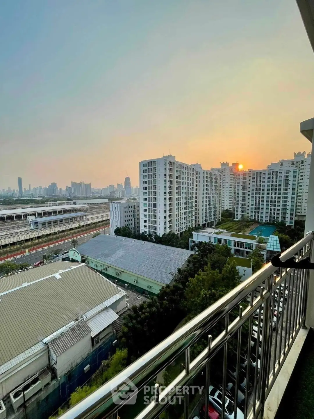 Stunning sunset view from a high-rise balcony overlooking cityscape and residential buildings.