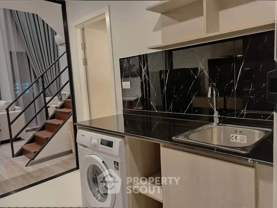 Modern duplex apartment with sleek kitchen and washing machine, featuring elegant black marble backsplash.