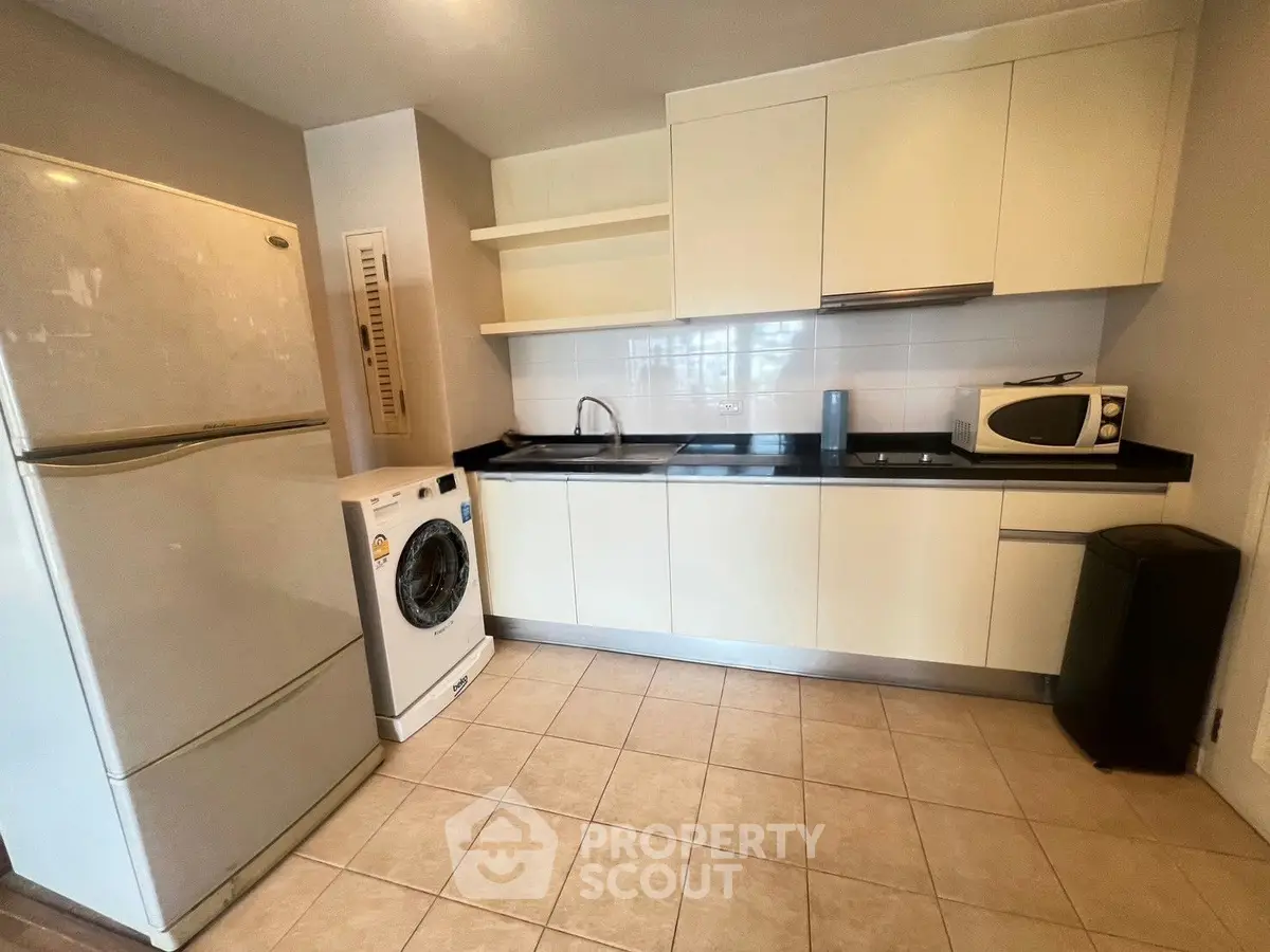 Modern kitchen with sleek cabinets, washing machine, fridge, and microwave in a compact layout.