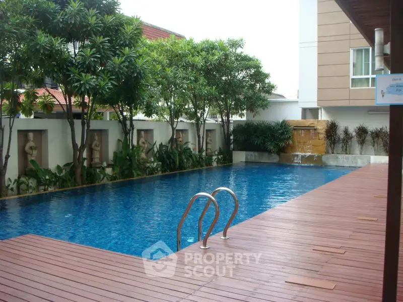 Luxurious outdoor swimming pool with wooden deck and lush greenery in modern residential area.