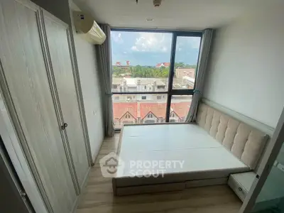 Modern bedroom with large window offering city view, featuring built-in wardrobe and air conditioning.