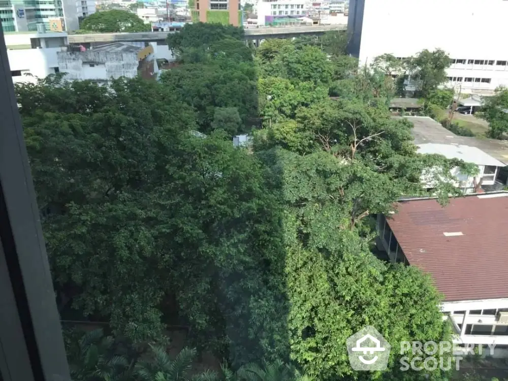 Lush green view from high-rise apartment window overlooking urban landscape.