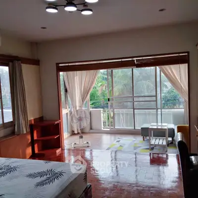 Spacious bedroom with large windows and balcony view, featuring elegant decor and natural light.