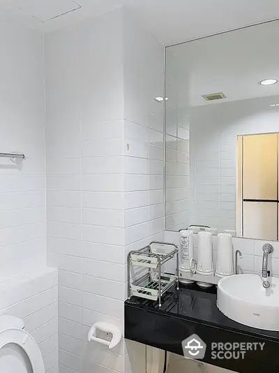 Pristine white-tiled bathroom featuring a sleek countertop basin, large mirror, and modern amenities, exuding a clean and minimalist aesthetic.