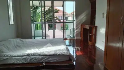 Spacious bedroom with polished wooden floors and large windows overlooking lush greenery.