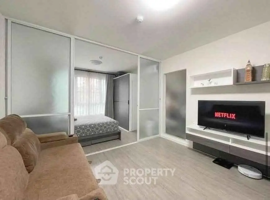 Modern living room with sliding doors and cozy bedroom view, featuring a large TV and comfortable seating.