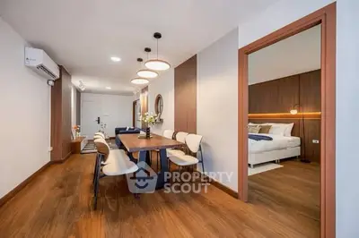 Modern dining area with wooden flooring and view into a cozy bedroom, featuring elegant lighting and decor.