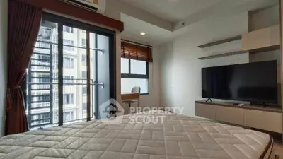 Modern bedroom with balcony access and large TV in a high-rise apartment.