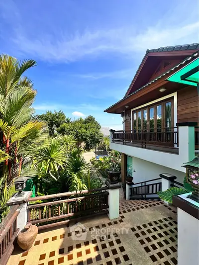 Charming tropical villa with lush garden and spacious balcony under clear blue sky.