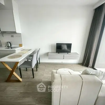 Modern living room with sleek furniture and open kitchen layout, featuring a cozy sofa and wall-mounted TV.