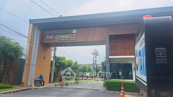 Modern gated community entrance with security booth and lush greenery.