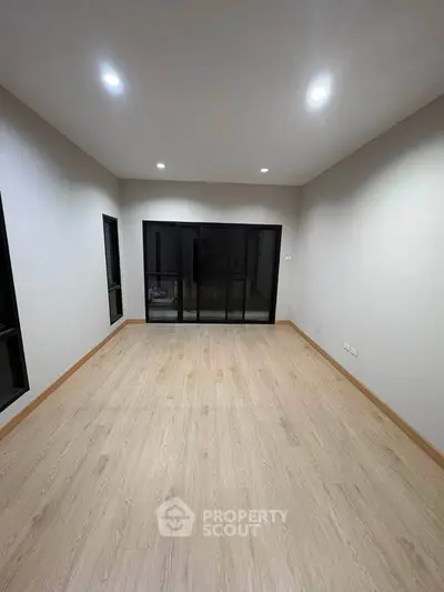 Spacious empty room with wooden flooring and large windows for natural light.