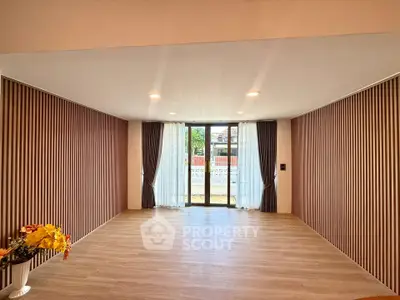 Spacious living room with wooden flooring and large windows opening to a garden view.