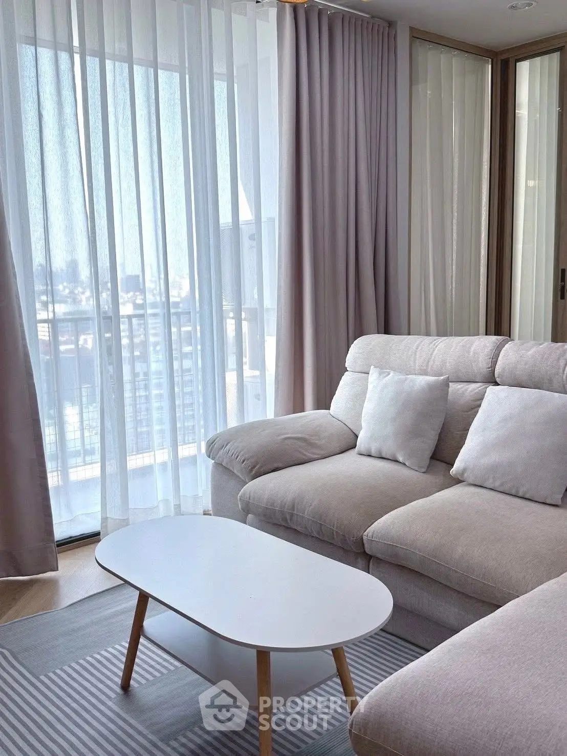 Modern living room with cozy beige sofa and city view from large windows.
