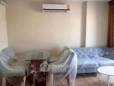 Modern living room with air conditioning and furniture covered in protective plastic.
