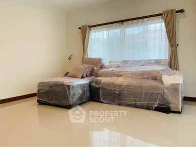 Spacious living room with wrapped furniture and large window, perfect for customization.