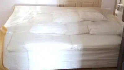 Spacious bedroom with a large bed wrapped in protective plastic, ideal for moving or storage.
