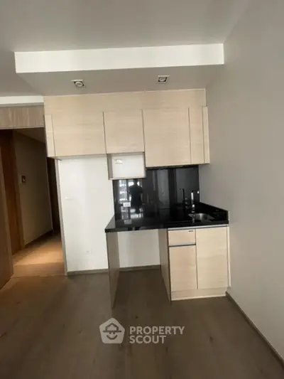 Modern minimalist kitchen with sleek cabinetry and black countertop in open layout apartment.