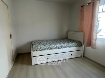 Cozy bedroom with single bed and floral bedding, soft lighting, and pink curtains.