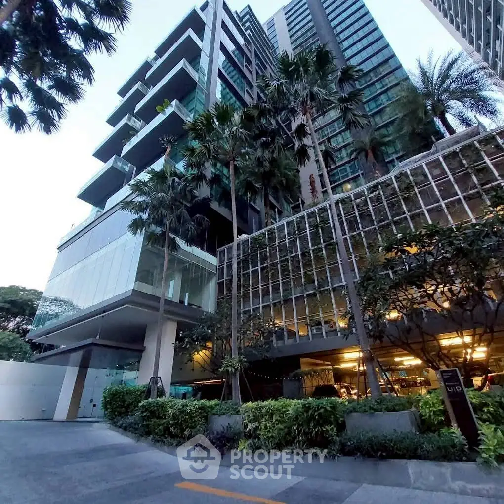 Modern high-rise building with lush greenery and glass facade in urban setting.