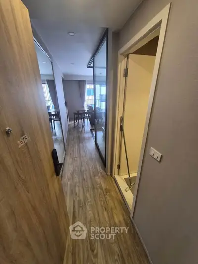 Modern apartment entrance with wooden flooring and glass partition leading to living area.