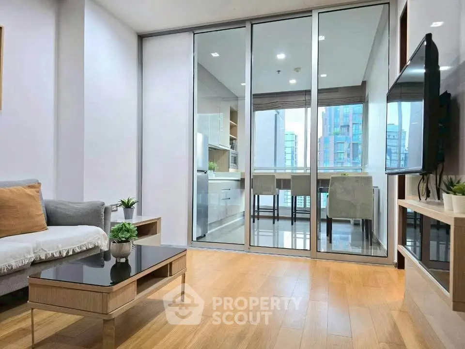 Modern living room with glass doors leading to a stylish dining area and city view.